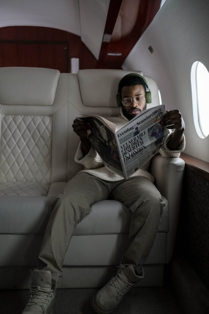 African American man reading newspaper and listening to music in airplane cabin with headphones.
